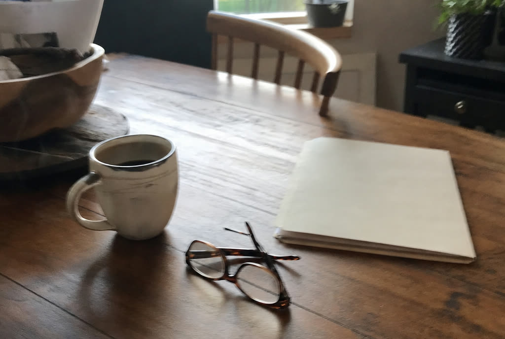 Taking the plan home: reading glasses, coffee, and the folder on a kitchen table